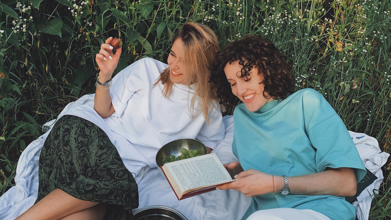 Two friends reading a book and having a picnic